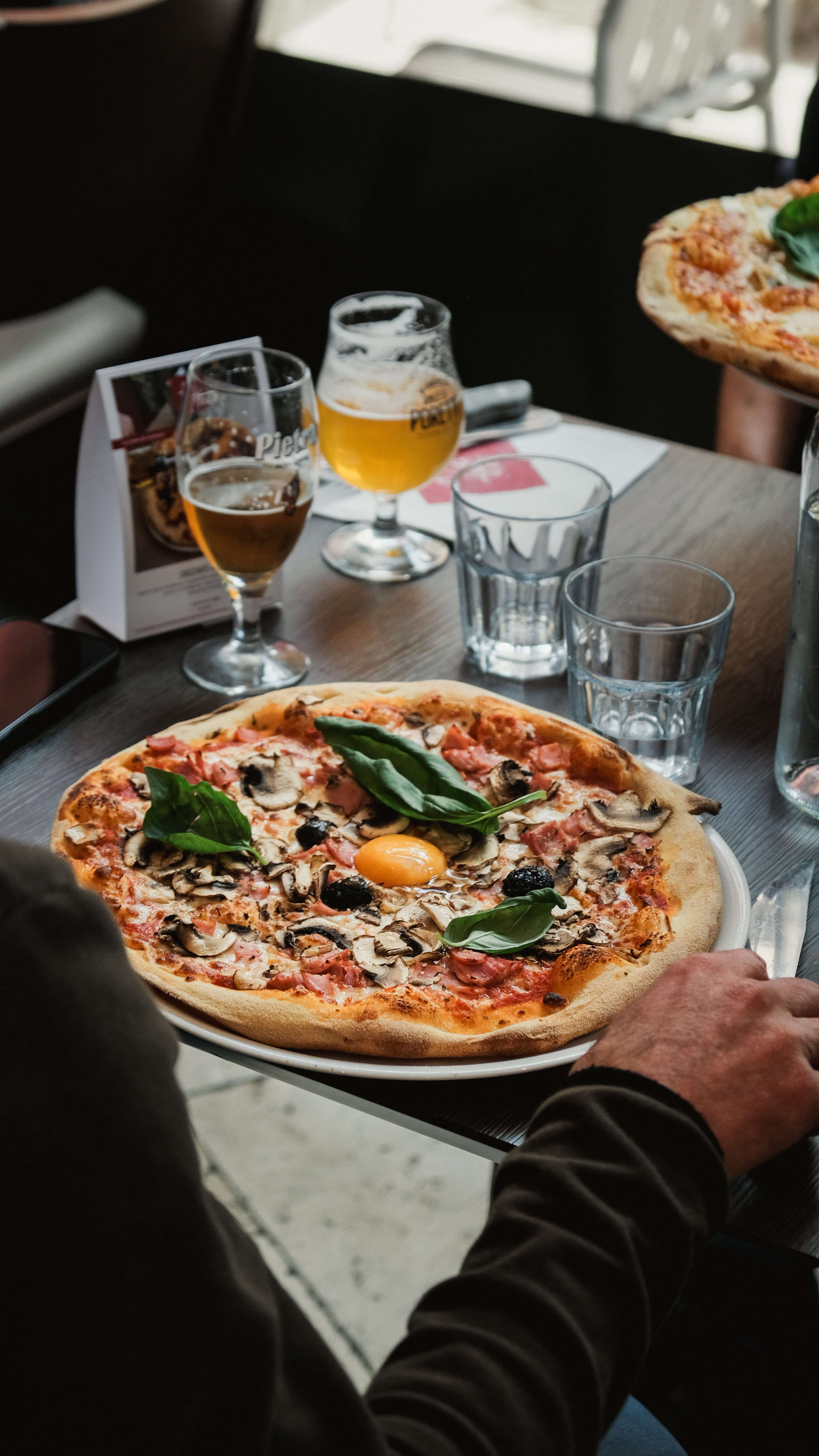 Pizza Fabioli garnie de champignons, jambon et œuf, servie en terrasse avec deux bières