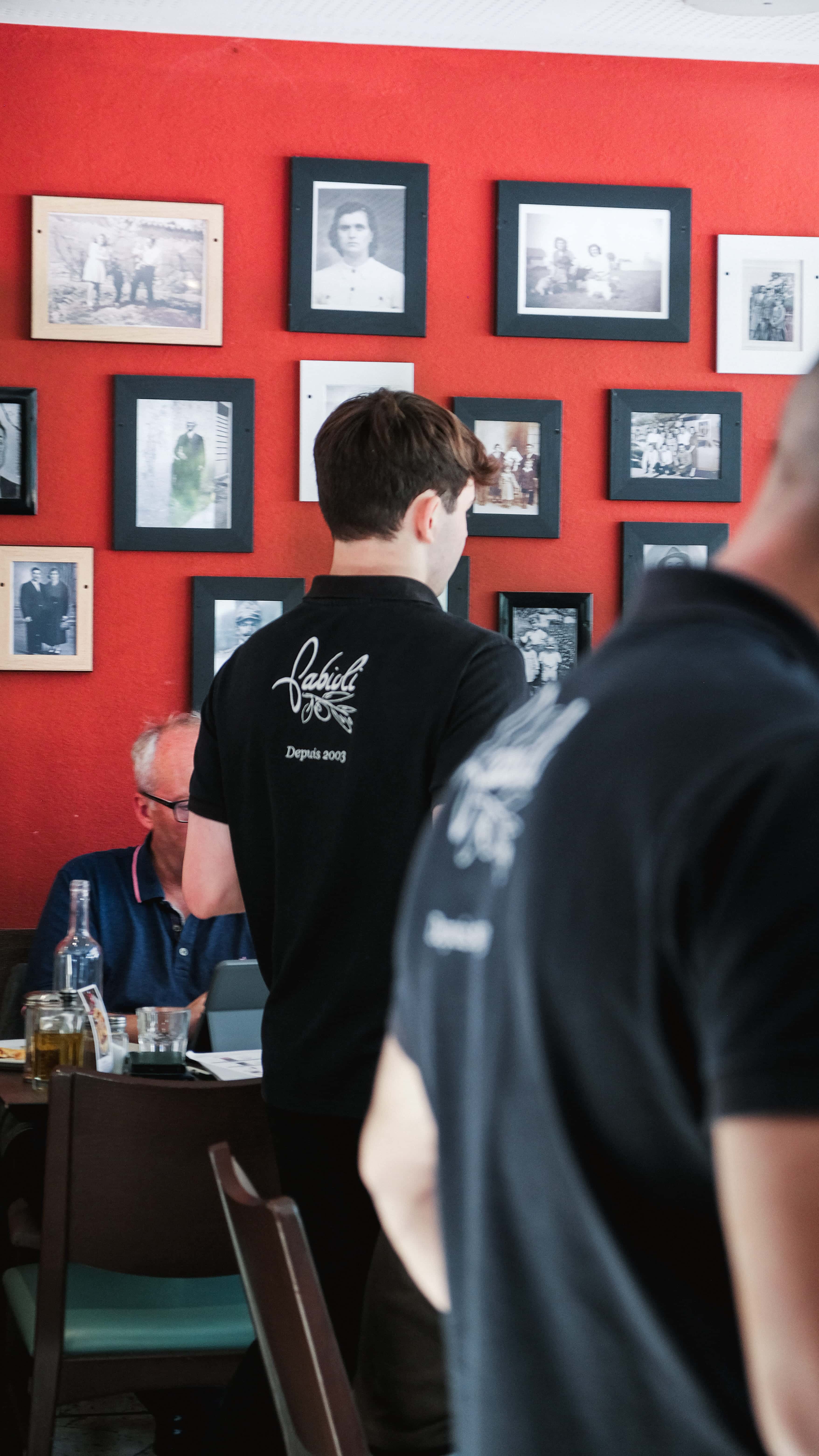Serveurs Fabioli en polo « Depuis 2003 » devant le mur de photos de famille